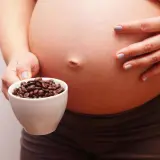 Una mujer embarazada sostiene una taza de granos de café. El café y el embarazo son un tema delicado.