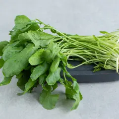 Un manojo fresco de el berro, con sus hojas verdes vibrantes y tallos delgados, descansa sobre una tabla oscura.