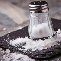 Salero de cristal con sal esparcida. La sal marina tiene yodo, esencial para la salud.