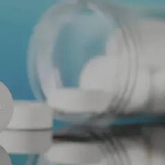 Pastillas de yodo blancas, una en primer plano con la palabra "IODINE" grabada, y un frasco volcado con más pastillas.