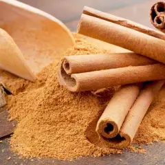 Palitos de canela y canela molida en una cuchara de madera. Descubre los 7 beneficios de la canela molida.