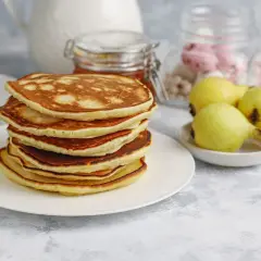 Pila de tortitas fit doradas y esponjosas, acompañadas de peras y un tarro de miel. Un desayuno saludable y delicioso.