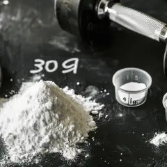 Montón de creatina en polvo, pesas y dosificador. La creatina por peso es clave para optimizar tu entrenamiento.