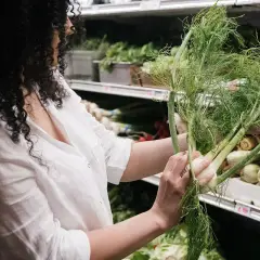 Mujer con cabello rizado elige hinojo fresco, reconociendo sus maravillosas propiedades para la salud.