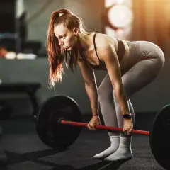 Mujer concentrada levanta una barra pesada, demostrando fuerza y dedicación en su entrenamiento para ganar masa muscular.