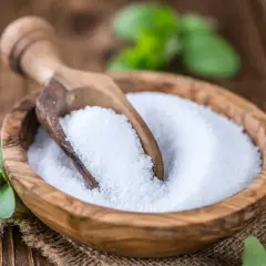 Tazón de madera con azúcar de stevia y cuchara. Las hojas verdes de stevia alrededor nos recuerdan que es la stevia, un edulcorante natural.