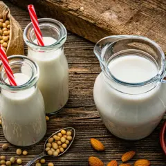 Botellas y jarra con bebida vegetal, junto a un saco de soja y almendras.