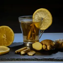 Un vaso de té con limón y jengibre, acompañado de rodajas de limón y trozos de jengibre fresco. Un shot de jengibre para revitalizar.