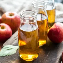 Botellas de vinagre de manzana, destacando sus propiedades naturales. Manzanas rojas frescas rodean el líquido dorado.