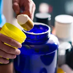 Man prepara su batido de creatina, iniciando la fase de carga con polvo blanco en un gran recipiente azul.