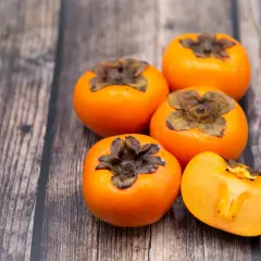 Caquis sobre una mesa de madera. Estos son algunos alimentos que estriñen, ¡pero deliciosos!
