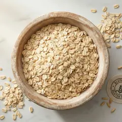Un cuenco de madera lleno de copos de avena, con algunos esparcidos alrededor. Un sello indica "Gluten-Free", pero la avena tiene gluten.