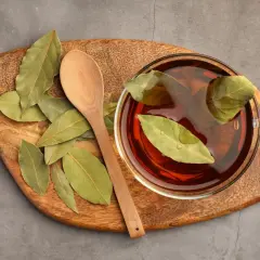 Taza de infusión de laurel con hojas flotando, junto a una cuchara de madera sobre una tabla rústica.