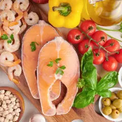 Salmón, camarones, almendras, garbanzos y aceitunas son algunos de los alimentos con yodo que se ven en la imagen, junto a tomates, pimientos y hierbas.