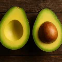 Dos mitades de aguacate sobre madera. Una sin hueso, la otra con su gran semilla marrón. ¡Un tesoro de grasas saludables y pocas calorías aguacate!