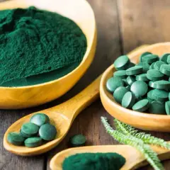 Polvo y pastillas verdes vibrantes, que muestran qué es la chlorella, en cuencos de madera y cucharas sobre una superficie rústica.
