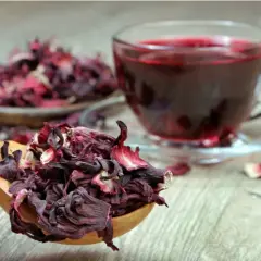 Cucharada de flor de jamaica seca junto a una taza de té rojo vibrante.