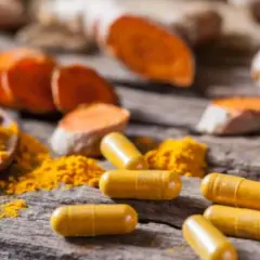 Cápsulas amarillas y polvo de cúrcuma sobre madera. Descubre cómo tomar cúrcuma en cápsulas para aprovechar sus beneficios.