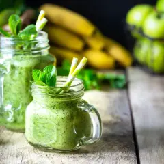 Batidos verdes refrescantes con espirulina, que es un superalimento, adornados con menta. Plátanos, naranjas y manzanas verdes en el fondo.