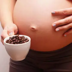 Una mujer embarazada sostiene una taza de granos de café. El café y el embarazo son un tema delicado.