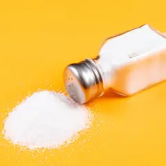 Salero volcado con sal yodada o normal derramada sobre fondo amarillo.