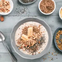 Un tazón de avena con plátano, almendras picadas, semillas de chía y miel. Aprende como tomar avena para un desayuno nutritivo.