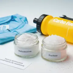 Dos frascos con maltodextrina y fructosa, junto a una camiseta azul y un bidón amarillo "Carbo Fuel". La maltodextrina es malo para tu rendimiento.