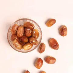 Un cuenco de cristal lleno de dátiles jugosos y otros esparcidos alrededor, destacando sus nutritivas propiedades.