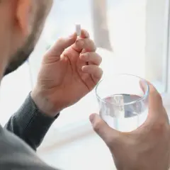 Hombre toma un comprimido de ácido fólico con un vaso de agua.