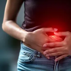 Persona con las manos en el abdomen, sintiendo un fuerte ardor de estómago. La zona afectada se ilumina en rojo.