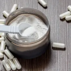 Cápsulas y polvo blanco sobre fondo de madera. La arginina es peligrosa, advierten las cápsulas esparcidas.