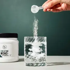 Un tarro de creatina monohidratada junto a un vaso donde se disuelve el polvo. Ideal para quienes buscan mejorar su rendimiento y apoyar la creatina para adelgazar.
