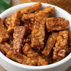 Trozos de tempeh que es, glaseados y dorados, servidos en un cuenco blanco.