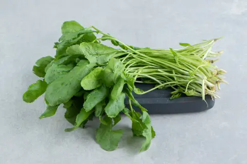 Un manojo fresco de el berro, con sus hojas verdes vibrantes y tallos delgados, descansa sobre una tabla oscura.