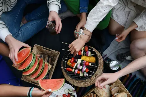 Disfrutando de una barbacoa vegetariana al aire libre con amigos, con brochetas de verduras a la parrilla, sandía y pan.