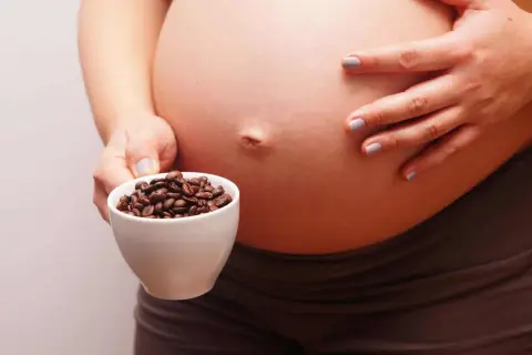 Una mujer embarazada sostiene una taza de granos de café. El café y el embarazo son un tema delicado.
