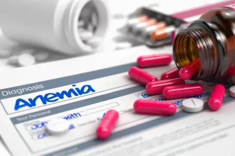 Pastillas rosas y blancas sobre un formulario de diagnóstico de anemia. Un frasco de suplemento de hierro derramado.