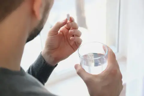 Hombre toma un comprimido de ácido fólico con un vaso de agua.
