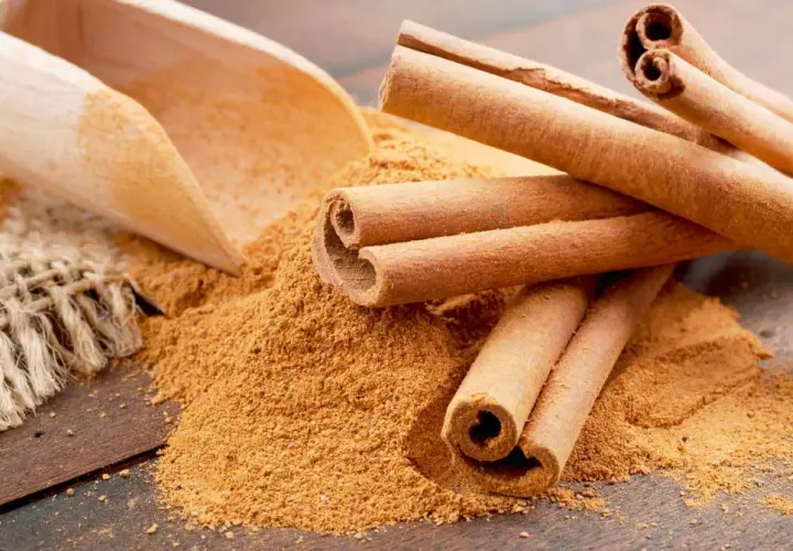 Palitos de canela y canela molida en una cuchara de madera. Descubre los 7 beneficios de la canela molida.