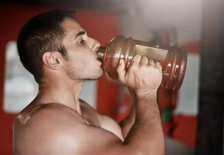 Hombre bebiendo de una gran botella, preparándose para un pre entreno fuerte.