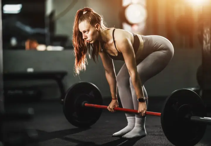 Mujer concentrada levanta una barra pesada, demostrando fuerza y dedicación en su entrenamiento para ganar masa muscular.