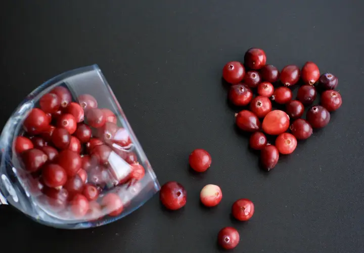 Arándanos rojos en forma de corazón y en una copa, ideales para infusiones y para saber para qué sirve la gayuba.