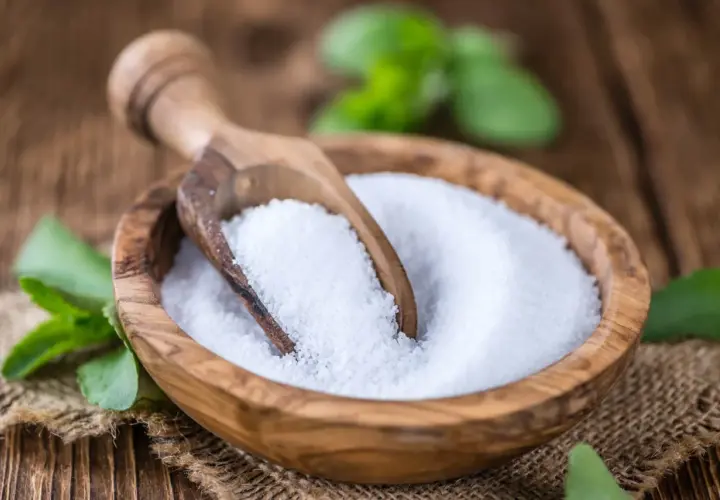 Tazón de madera con azúcar de stevia y cuchara. Las hojas verdes de stevia alrededor nos recuerdan que es la stevia, un edulcorante natural.