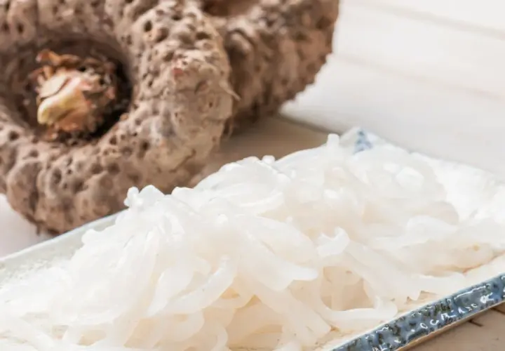 Raíz de konjac que es: un tubérculo grande y fibroso junto a un plato de fideos translúcidos hechos de konjac.