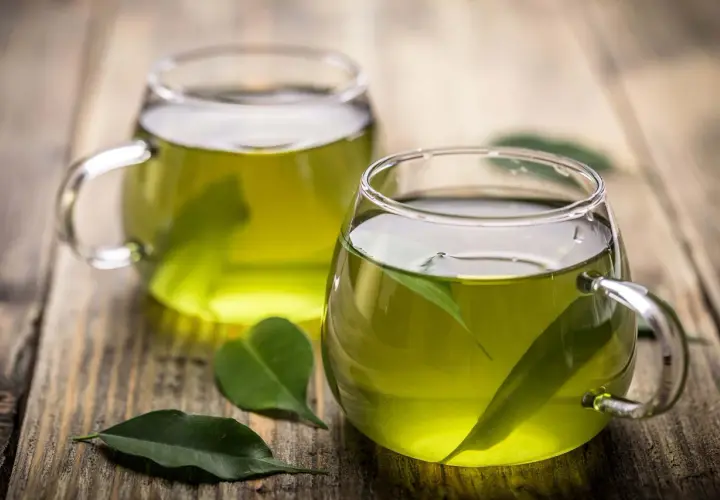 Dos tazas de té verde en vasos de cristal, con hojas flotando. Descubre para qué sirve el té verde y sus beneficios.