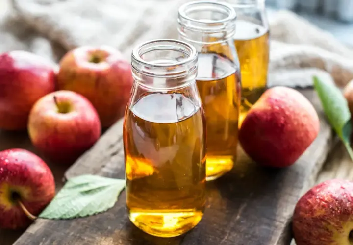 Botellas de vinagre de manzana, destacando sus propiedades naturales. Manzanas rojas frescas rodean el líquido dorado.