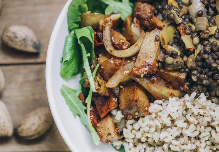 Un plato con seitan que es una proteína vegetal deliciosa, lentejas, arroz integral y hojas verdes.