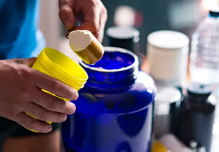 Man prepara su batido de creatina, iniciando la fase de carga con polvo blanco en un gran recipiente azul.