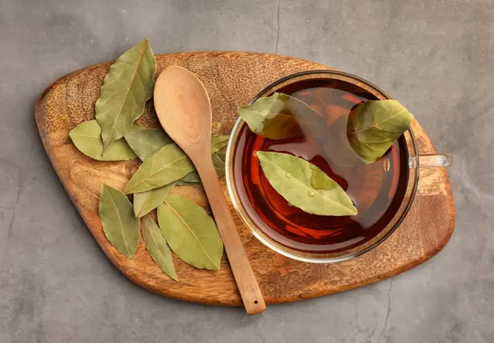 Taza de infusión de laurel con hojas flotando, junto a una cuchara de madera sobre una tabla rústica.