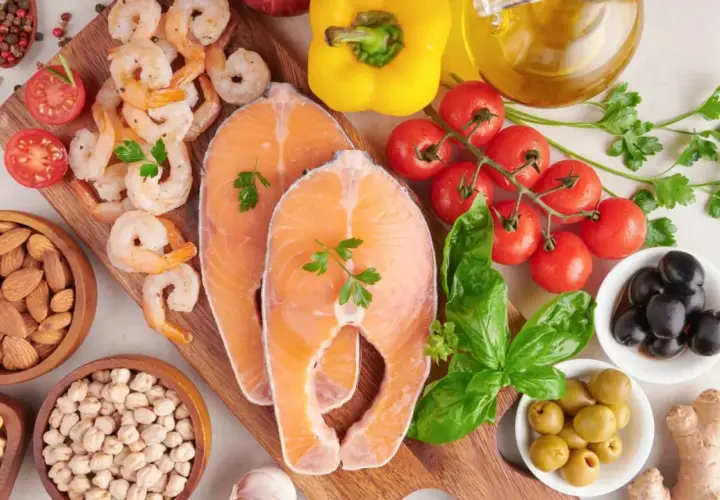 Salmón, camarones, almendras, garbanzos y aceitunas son algunos de los alimentos con yodo que se ven en la imagen, junto a tomates, pimientos y hierbas.